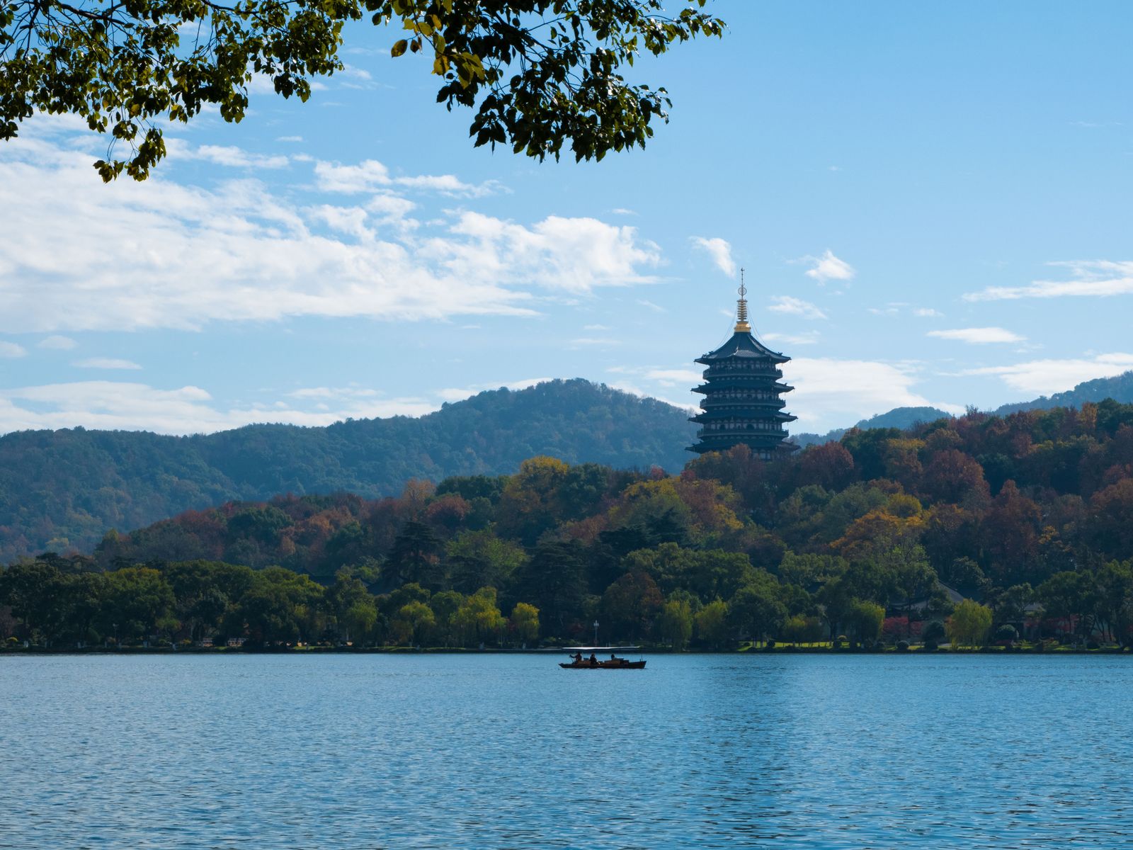 Leifeng Pagoda framed by autumn foliage above the waters of West Lake in Hangzhou, with green hills behind the lake