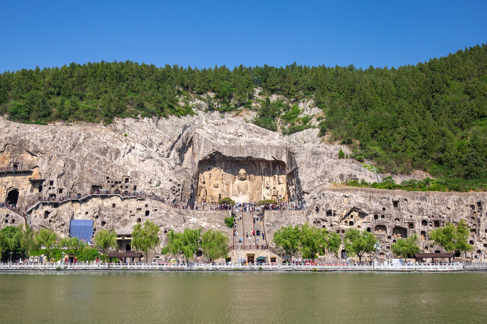 The Longmen Grottoes in Luoyang: Buddhist statues and niches carved into a limestone cliff along the Yi River under a clear blue sky